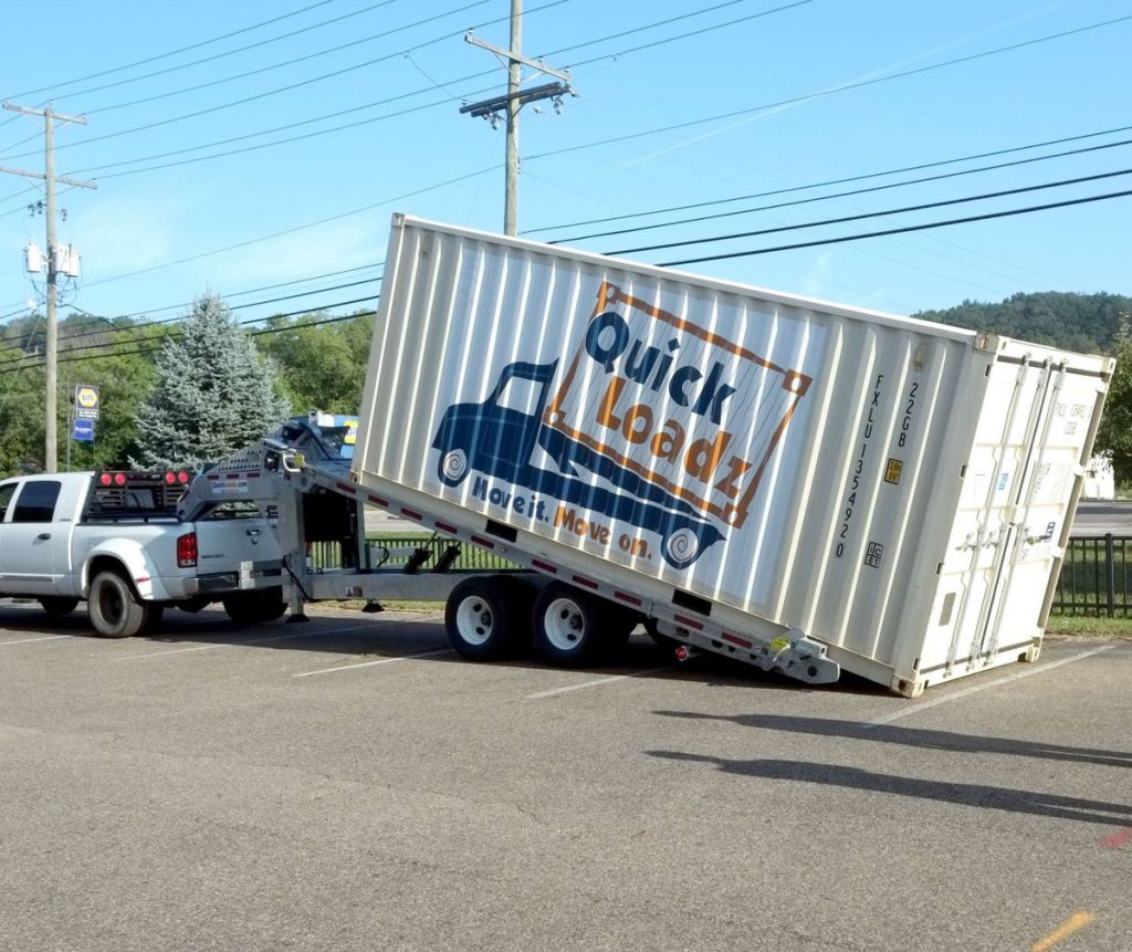 A QuickLoadz automated trailer at an angle with a sea shipping container loaded. The container has the QuickLoadz logo on the side.