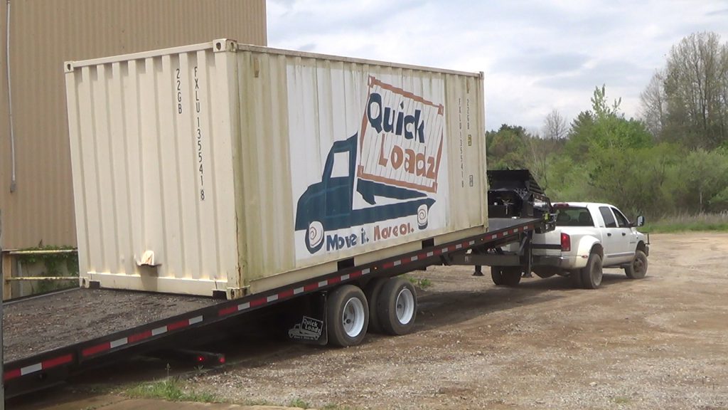 The QuickLoadz 26k Super 40 at an angle with a 20 foot container halfway down the bed. The container has the QuickLoadz logo painted on the side.