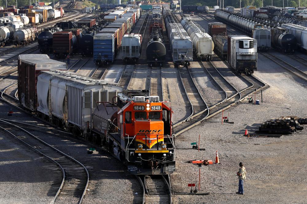 Train leaving lot with lines of containers in the background. 